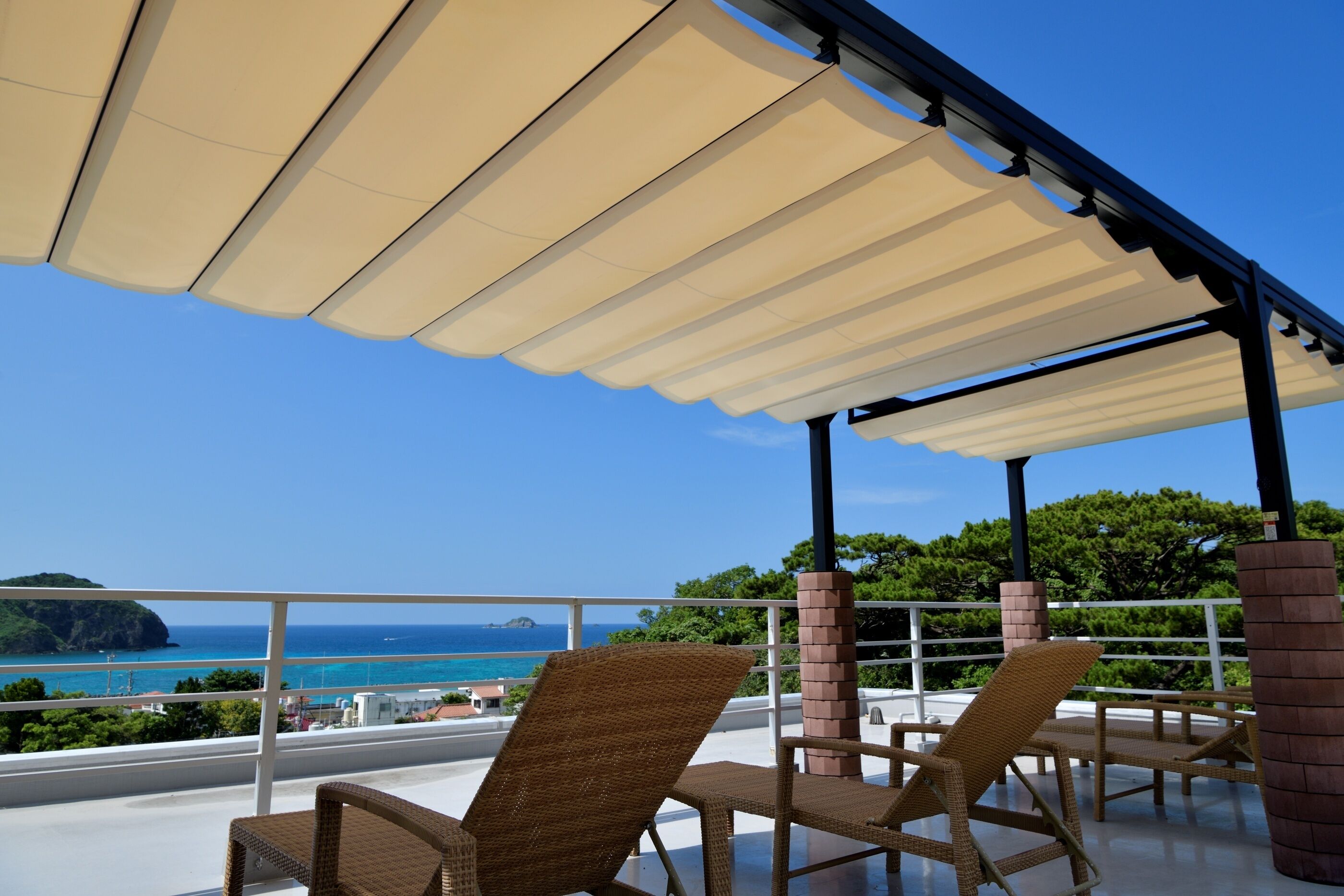 A covered outdoor seating area with wicker chairs and a view of the sea.