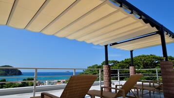A covered outdoor seating area with wicker chairs and a view of the sea.