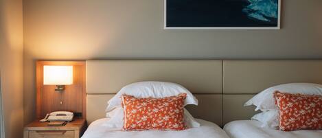 Habitación de hotel con dos camas, una mesita de noche, una lámpara, un cuadro en la pared y una revista sobre la cama.