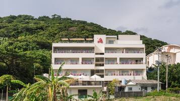 A multi-story hotel with balconies, surrounded by greenery and hills.