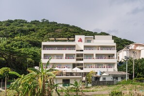 A multi-story hotel with balconies, surrounded by greenery and hills. - AKA LODGE by THE TERRACE HOTELS (Zamami)