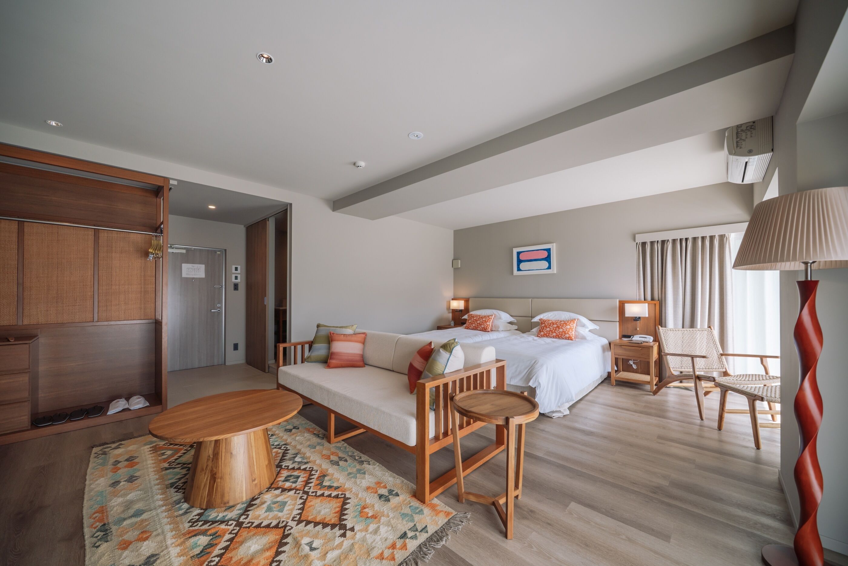 Ein Hotelzimmer mit einer Couch, zwei Betten, einem Holzstuhl, einem kleinen Tisch und einem gemusterten Teppich.