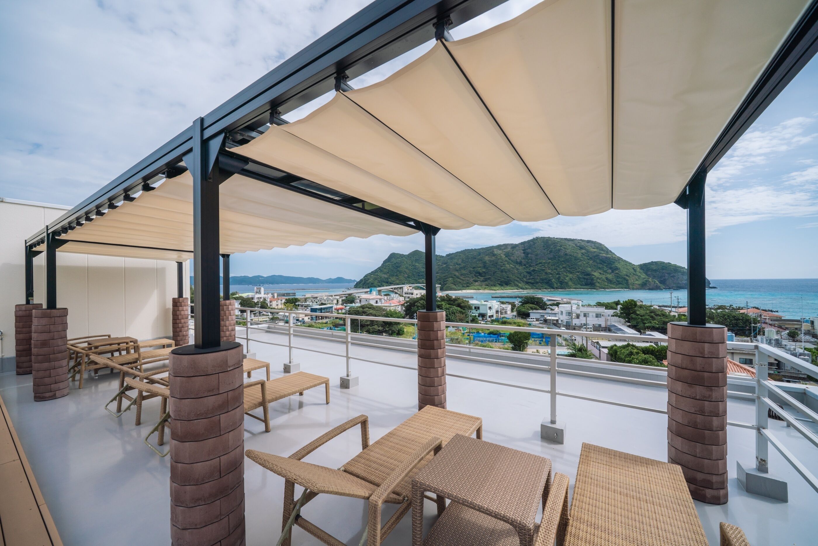 Een overdekt terras met rieten meubels en uitzicht op zee en heuvels.