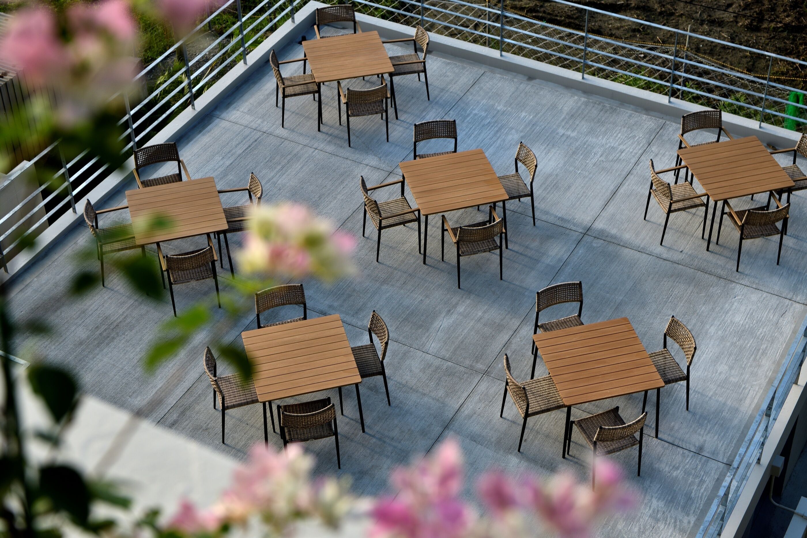 A rooftop patio with multiple tables and chairs, surrounded by a metal railing.