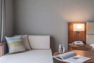 Habitación de hotel con cama, mesita de noche con lámpara, teléfono y vaso de agua.