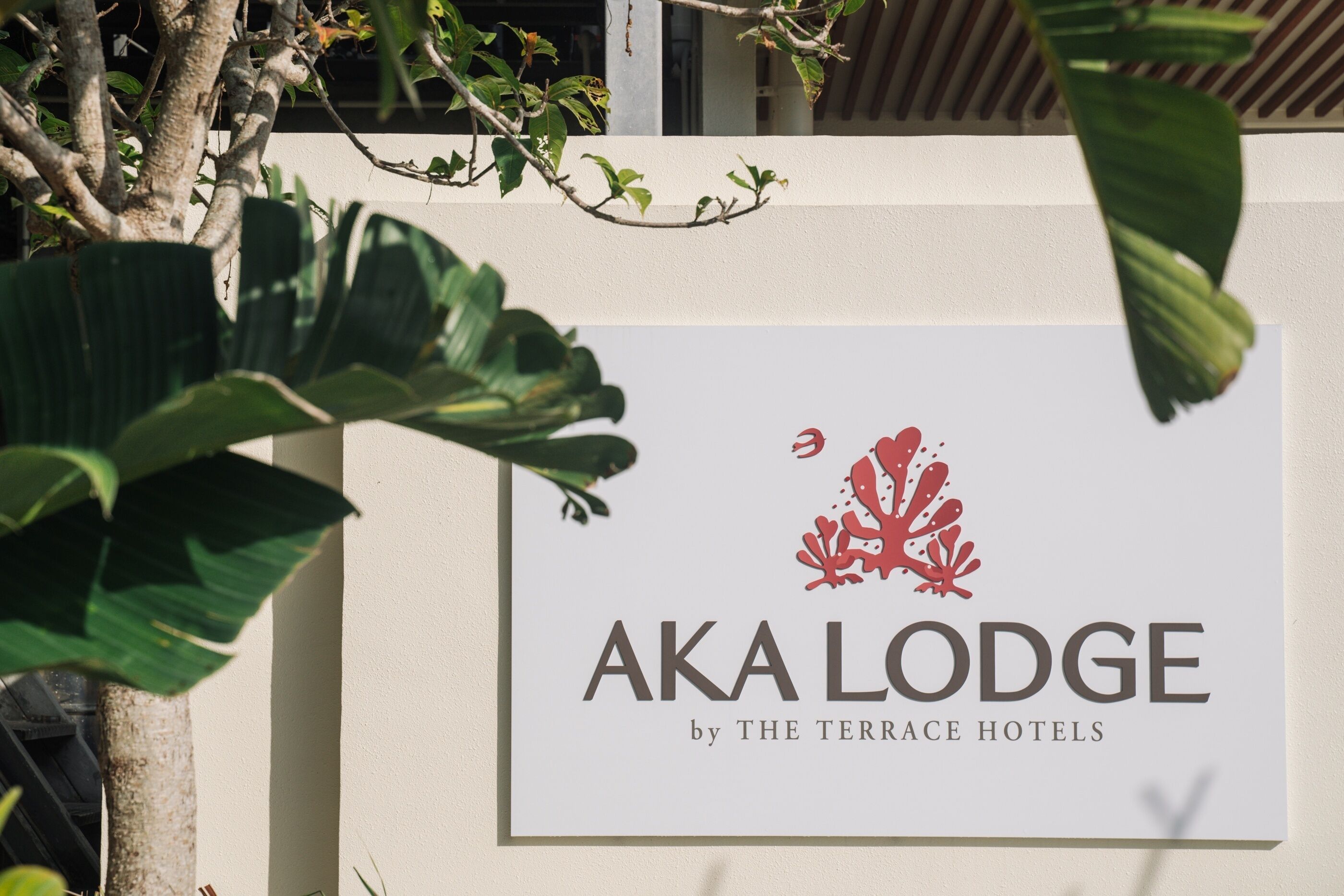 Une enseigne pour « AKA LODGE by THE TERRACE HOTELS », avec un motif graphique en forme de corail rouge.