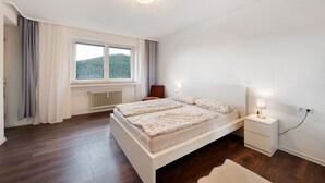 Une chambre à coucher avec un grand lit, des tables de chevet, une fenêtre avec des rideaux et un radiateur.