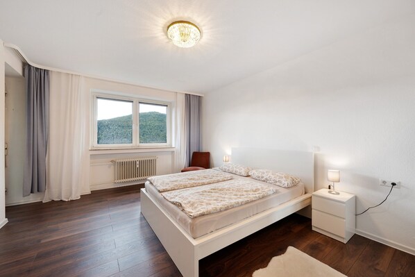Une chambre à coucher avec un grand lit, des tables de chevet, une fenêtre avec des rideaux et un radiateur.