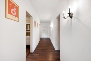 Un couloir avec un plancher en bois, des murs blancs et un panneau encadré sur le côté gauche.