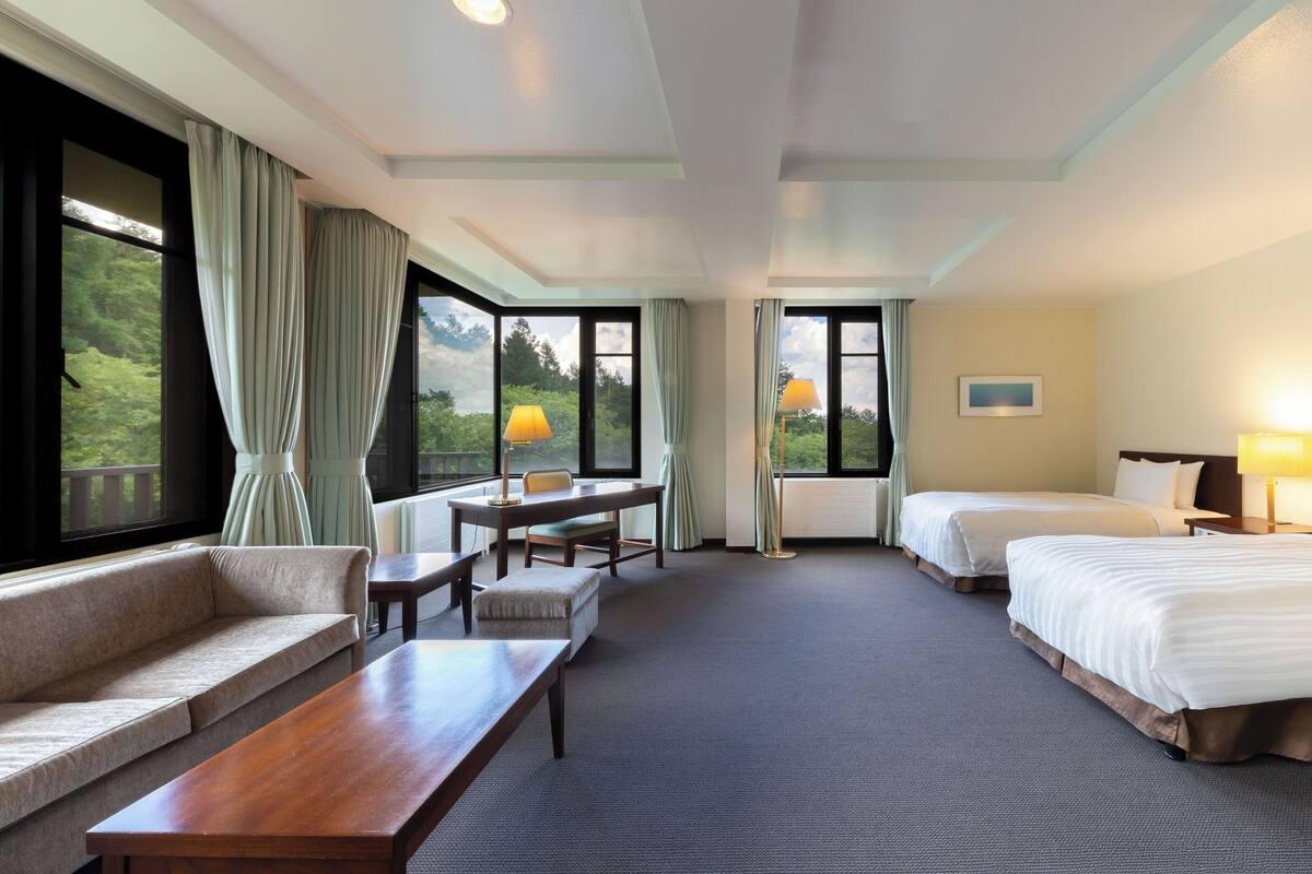 A hotel room with a sofa, a wooden table, two beds, and a desk.