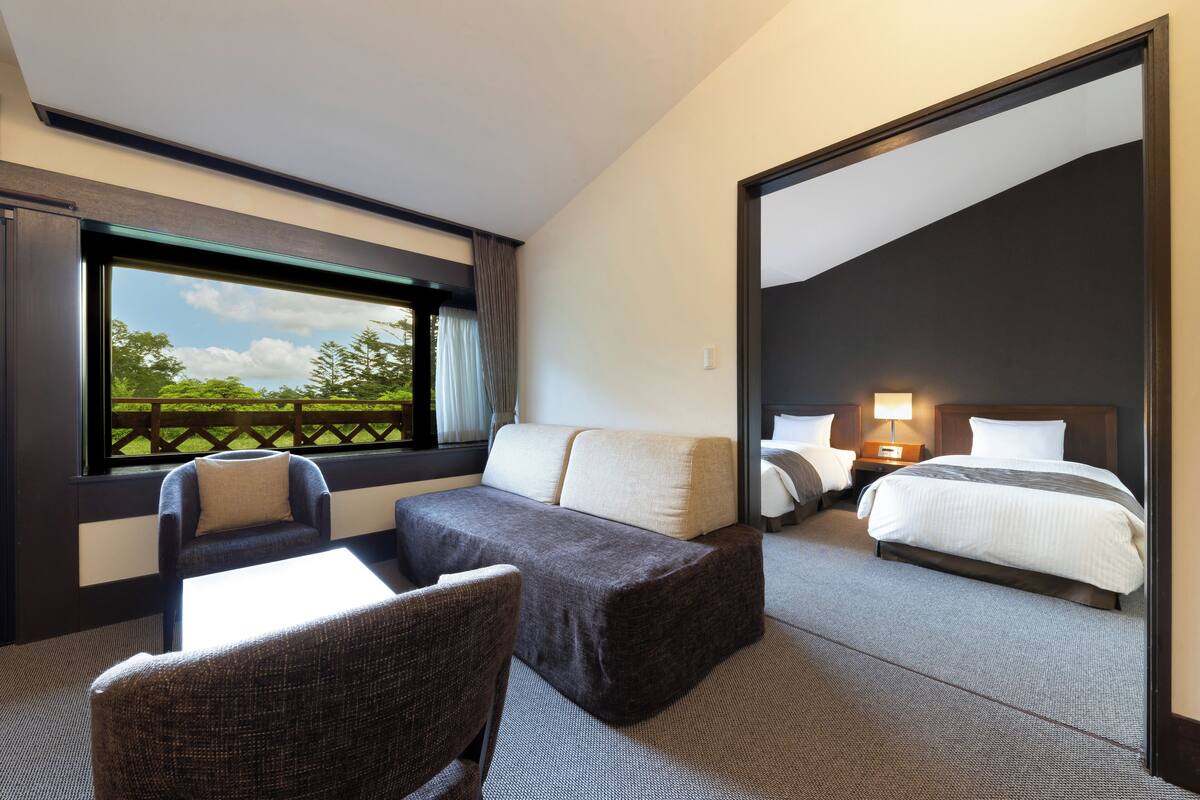 A hotel room with a sofa, a chair, a bed, and a view of the outdoors.