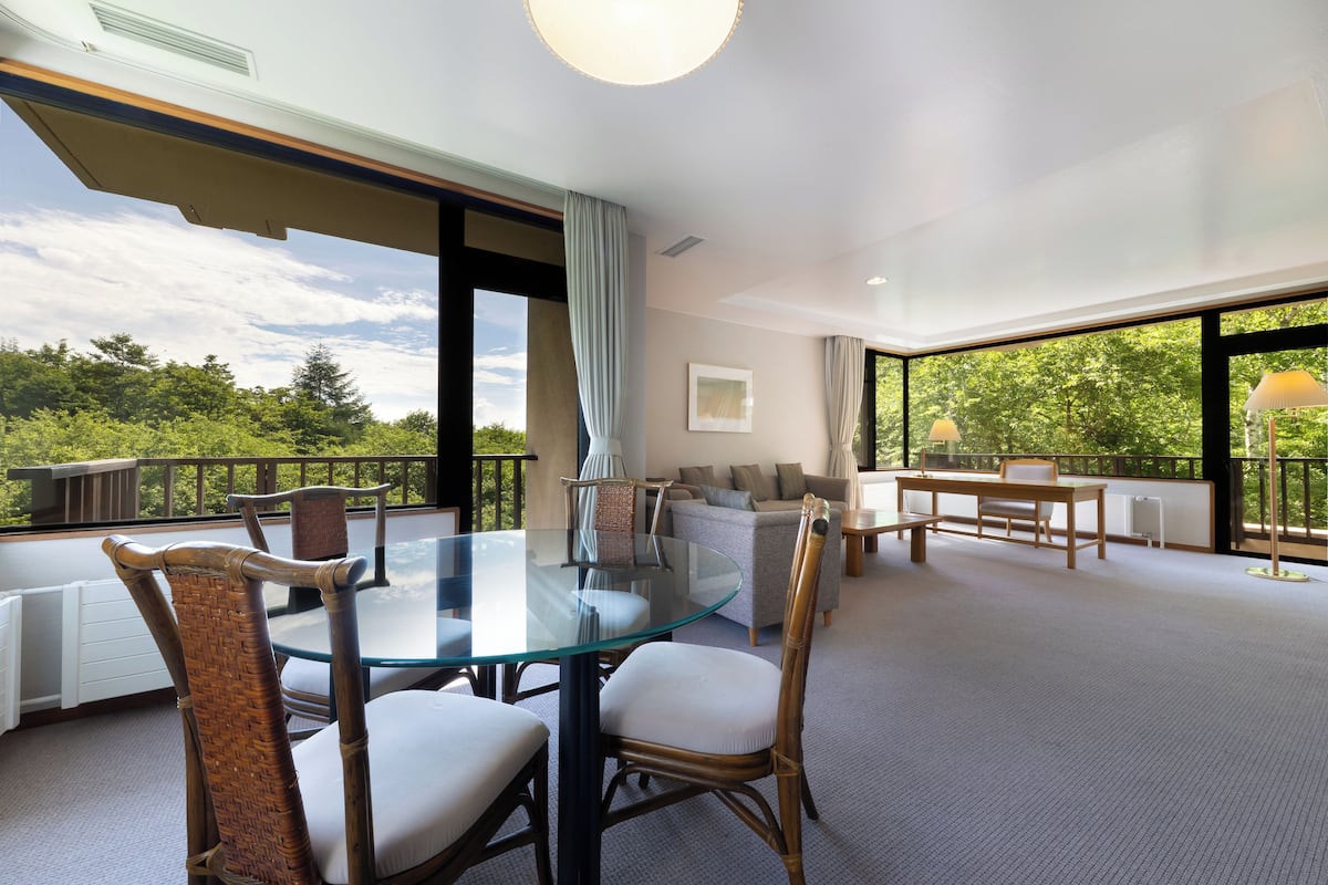 A spacious balcony with a glass table and wicker chairs, overlooking a lush green landscape.