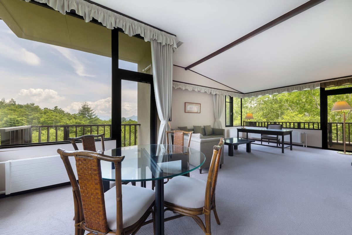 A spacious balcony with a glass table and chairs, a sofa, and a dining table.