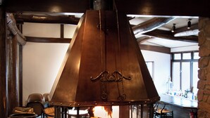 A stone fireplace with a metal chimney, surrounded by chairs and a bar area.