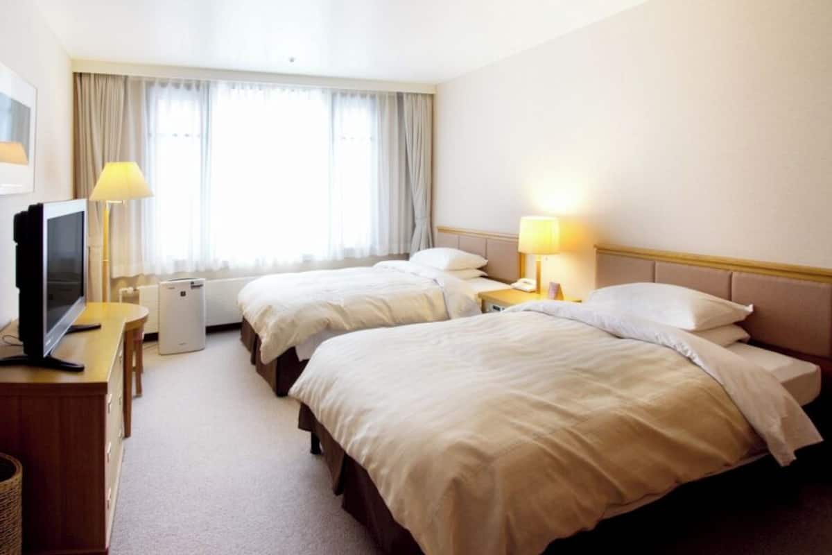A hotel room with two beds, a desk with a TV, a lamp, and a window with curtains.