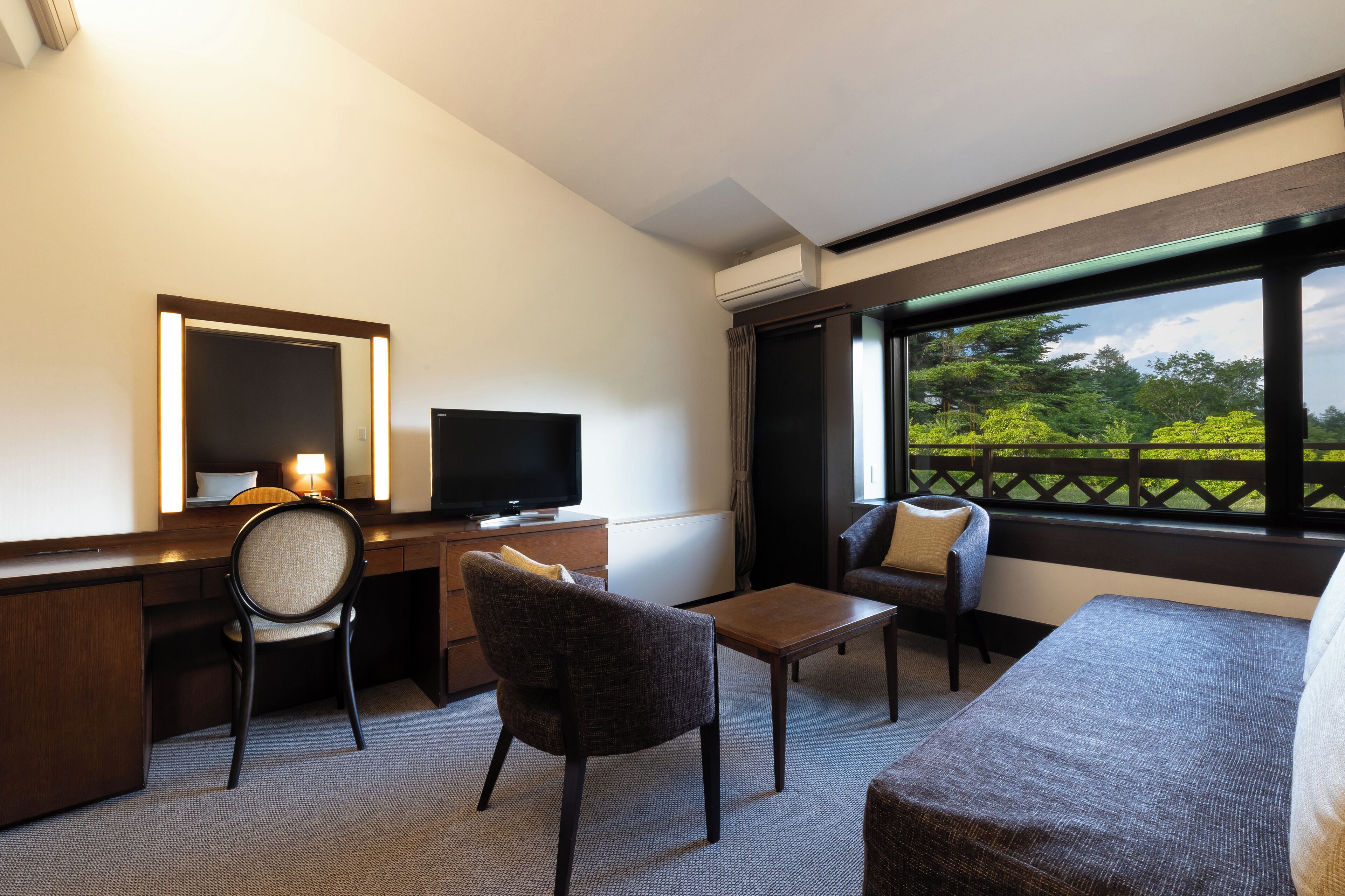 Een hotelkamer met een bureau, stoel, televisie en een bank.