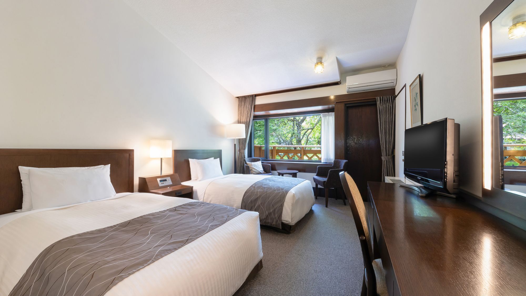 Ein Hotelzimmer mit zwei Betten, einem Schreibtisch, einem Fernseher und einem Fenster mit Blick auf Grünflächen.