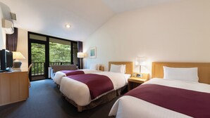 A hotel room with three beds, a desk with a computer, a TV, and a balcony with a view of trees. - Yatsugatake Kogen Lodge (Minamimaki)