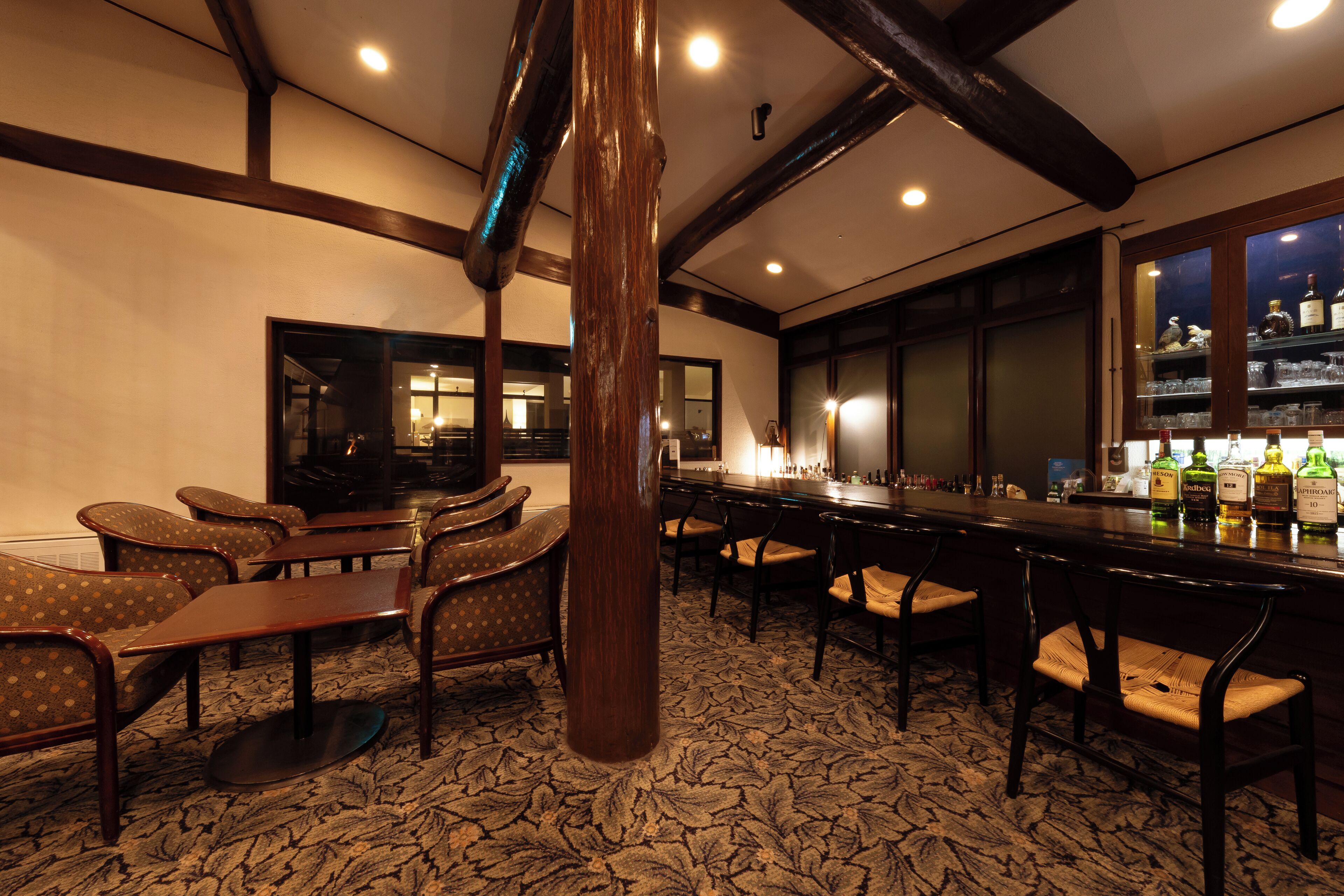 A bar area with wooden furniture, a patterned carpet, and a bar stocked with bottles.