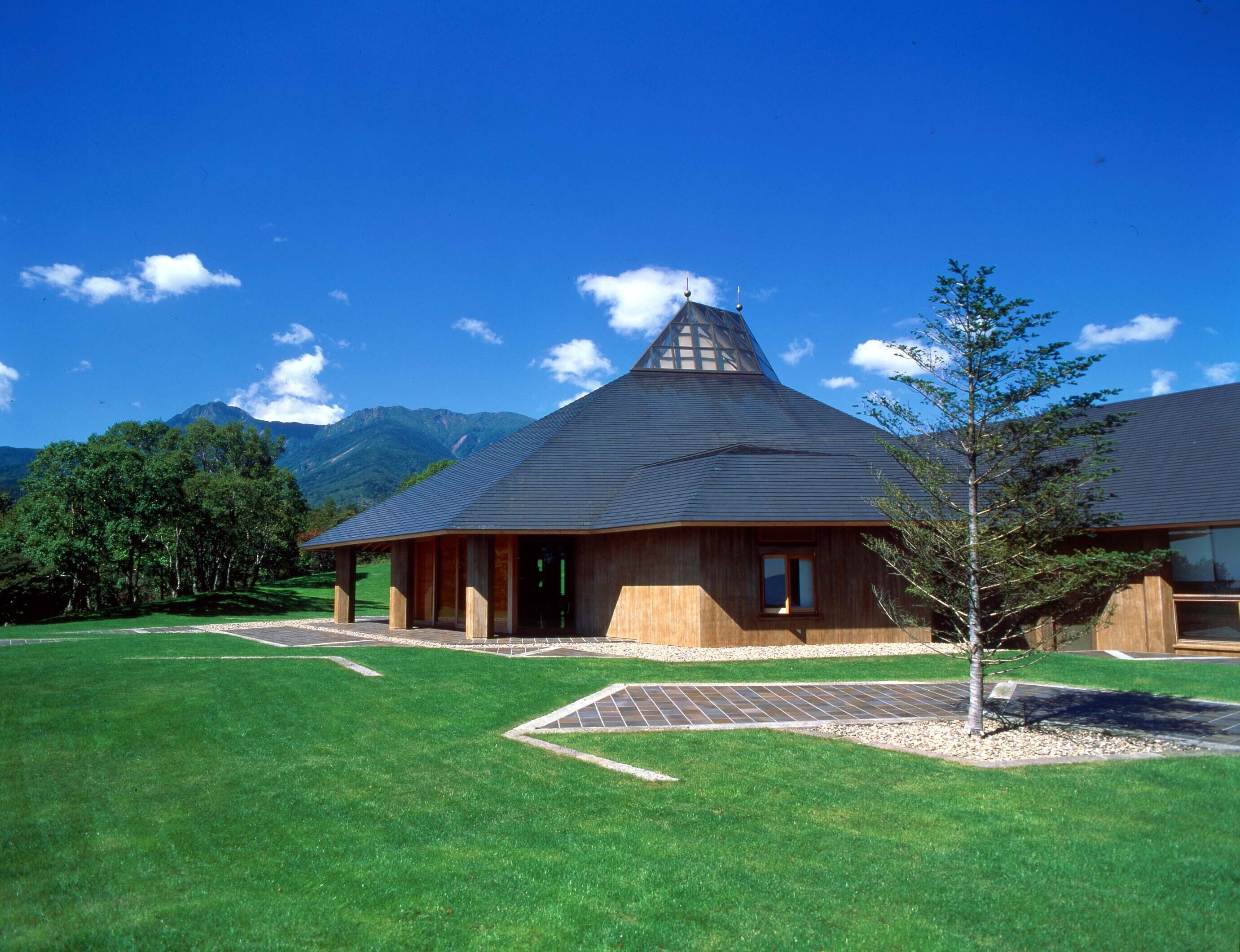A modern building with a sloped roof, surrounded by a well-maintained lawn and a small tree.