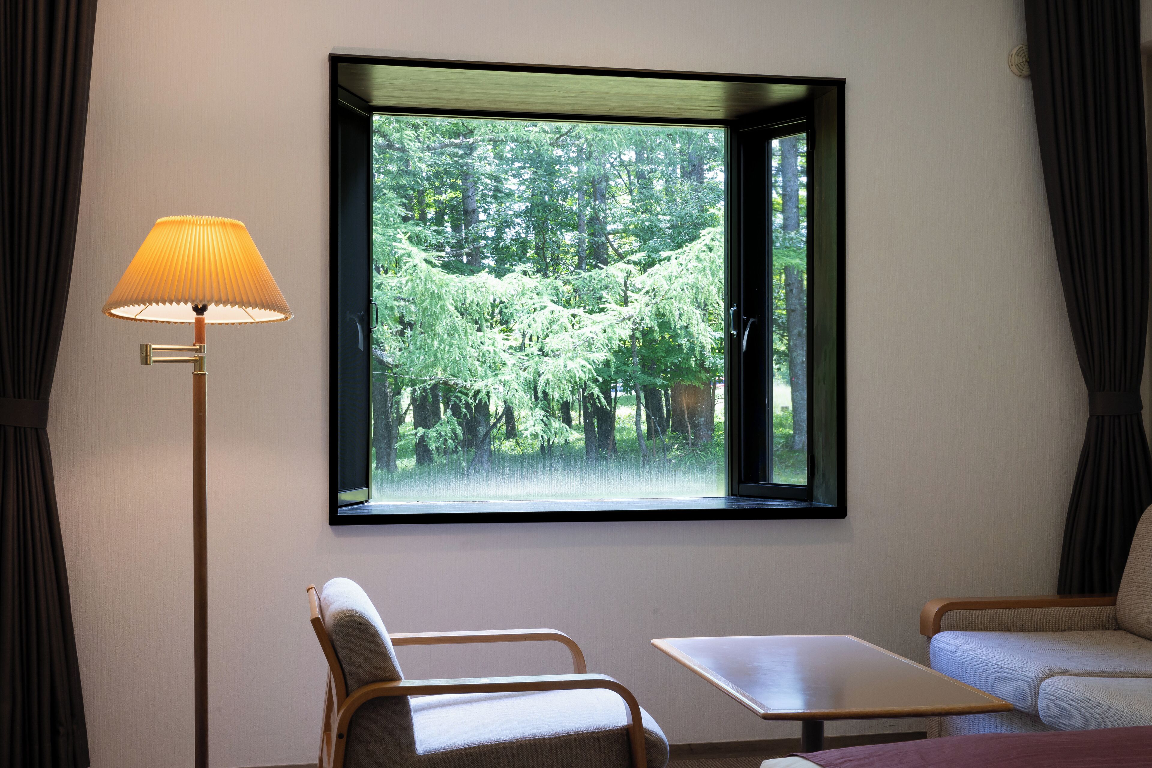 A room with a window, a lamp, a chair, and a sofa.