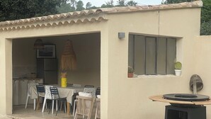 A covered outdoor dining area with a table and chairs, a hanging light fixture, and a small window with a potted plant. - Charming villa in Provence (Piolenc)