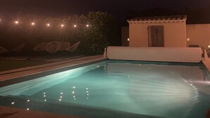 A swimming pool at night with string lights overhead. - Charming villa in Provence (Piolenc)