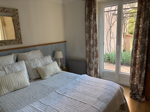 Un dormitorio con cama, almohadas, una mesita de noche, lámpara y ventana con cortinas.