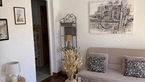 En hyggelig stue med trægulv, et rundt bord med en vase og en tallerken, en sofa med mønstrede puder og et billede på væggen.