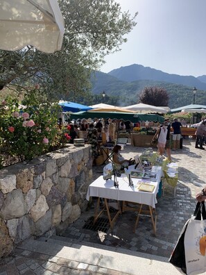 An outdoor market with tables displaying goods, surrounded by stone walls and greenery. - La Maison Victoire - Roquebillière (Roquebillière)