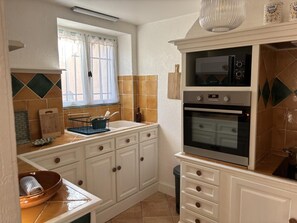 Una cocina con armarios blancos, horno empotrado y una ventana con cortinas.