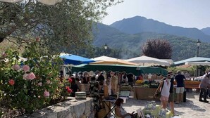 Un marché en plein air, avec des étals et des parasols, entouré de murs de pierre et de verdure.