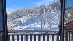 A view from a balcony with a metal railing, overlooking a snowy landscape with buildings and a ski lift. - Les Castors - ROUBION (ROUBION)