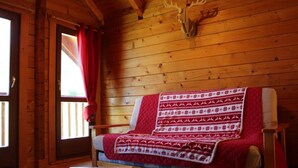 A cozy cabin room with a wooden interior, a bed with a red and white patterned blanket, a wooden table, and a deer head mounted on the wall. - Les Castors - ROUBION (ROUBION)