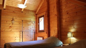 A wooden cabin room with two beds, a hanging light fixture, a window, and a floor lamp. - Les Castors - ROUBION (ROUBION)