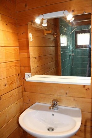 A wooden cabin bathroom with a white sink, a mirror, and a shower area. - Les Castors - ROUBION (ROUBION)