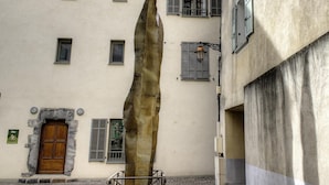 En bygning med en stor stenskulptur foran, en trædør med stenkarm og flere vinduer med skodder.