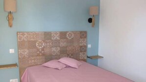 A bedroom with a patterned headboard, a pink bedspread, two bedside lamps, and a small wooden shelf.