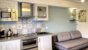 A compact kitchen with a microwave, oven, and sink. There is a sofa and a lamp in the adjacent living area.