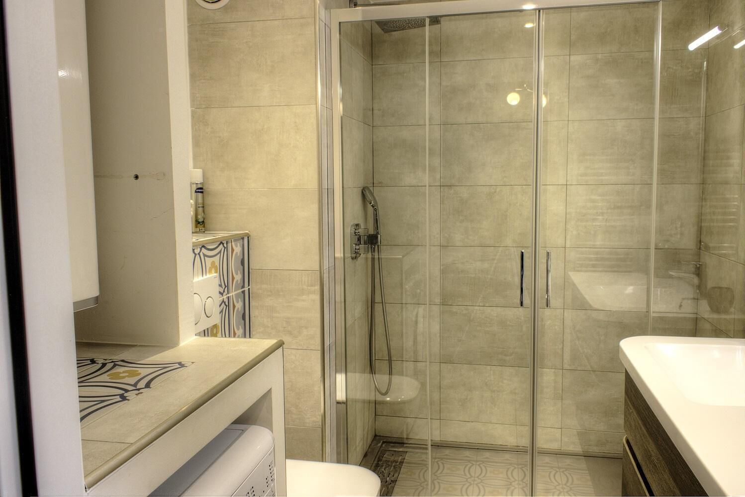 A modern bathroom with a glass-enclosed shower, a white sink, and a vanity with a patterned countertop.