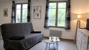 Ein Wohnzimmer mit grauem Sofa, einem kleinen runden Tisch mit Tassen und einem Fernseher auf einer Holzkommode.