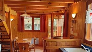 A wooden cabin interior with a dining area, kitchen, and a staircase.