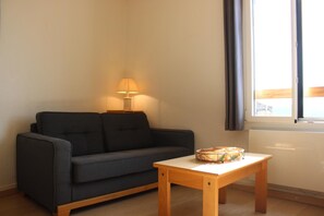 Una sala de estar con un sofá gris oscuro, una mesita de madera con un objeto decorativo, una lámpara y una ventana con cortinas.