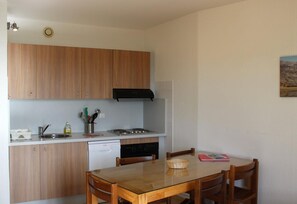 Una cocina compacta con armarios de madera, lavavajillas, estufa y una mesa de comedor con sillas.