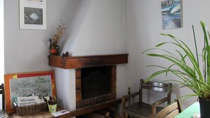 A corner room with a fireplace, a wooden bench, a table with a basket, and a potted plant. - La Maison Commune - CAILLE (CAILLE)