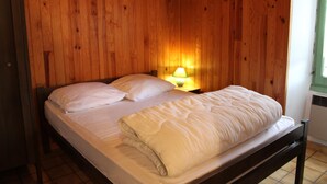 A single bed with white bedding in a room with wooden panel walls and a nightstand with a lamp. - La Maison Commune - CAILLE (CAILLE)