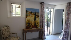 A bedroom with a bed, a chair, a painting, a window, and a door leading to a balcony. - L'Olivier de St Paul (SAINT-PAUL-DE-VENCE)