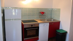 Una cocina compacta con refrigerador, estufa, horno, pileta y basurero.
