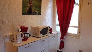 Una kitchenette con cafetera, microondas y hervidor sobre una encimera blanca.