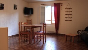 Una habitación con una mesa de comedor, sillas, un televisor, una ventana con cortinas y un adorno en la pared.